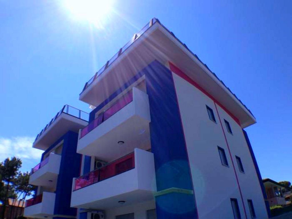 Un edificio de varios pisos con balcones, cielo despejado y sol brillante.