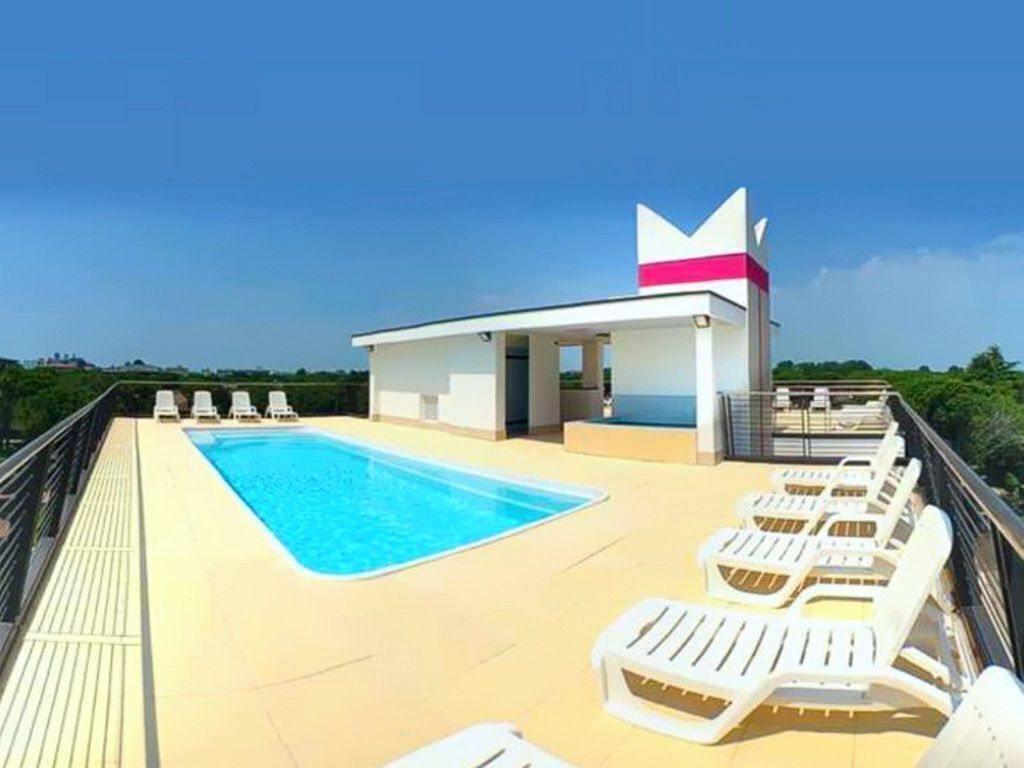 A rooftop pool with lounge chairs and a small building with a pink stripe.