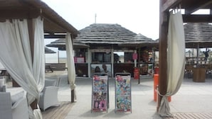 A beachside kiosk with a thatched roof, surrounded by beach chairs and umbrellas.