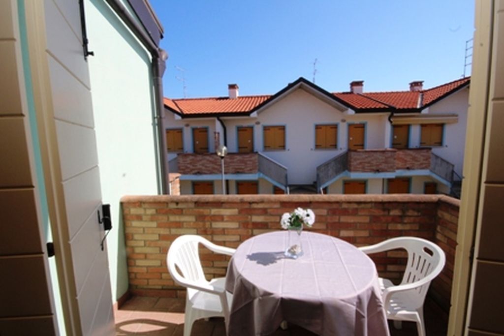 A patio with a round table and two white chairs, a brick wall, and a view of a building with red-tiled roofs.