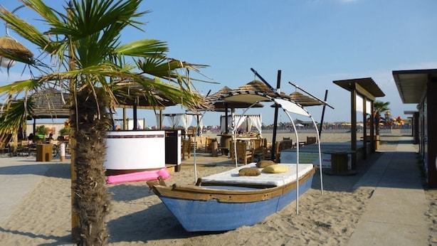 A beach with a small boat, palm trees, and beachside structures.