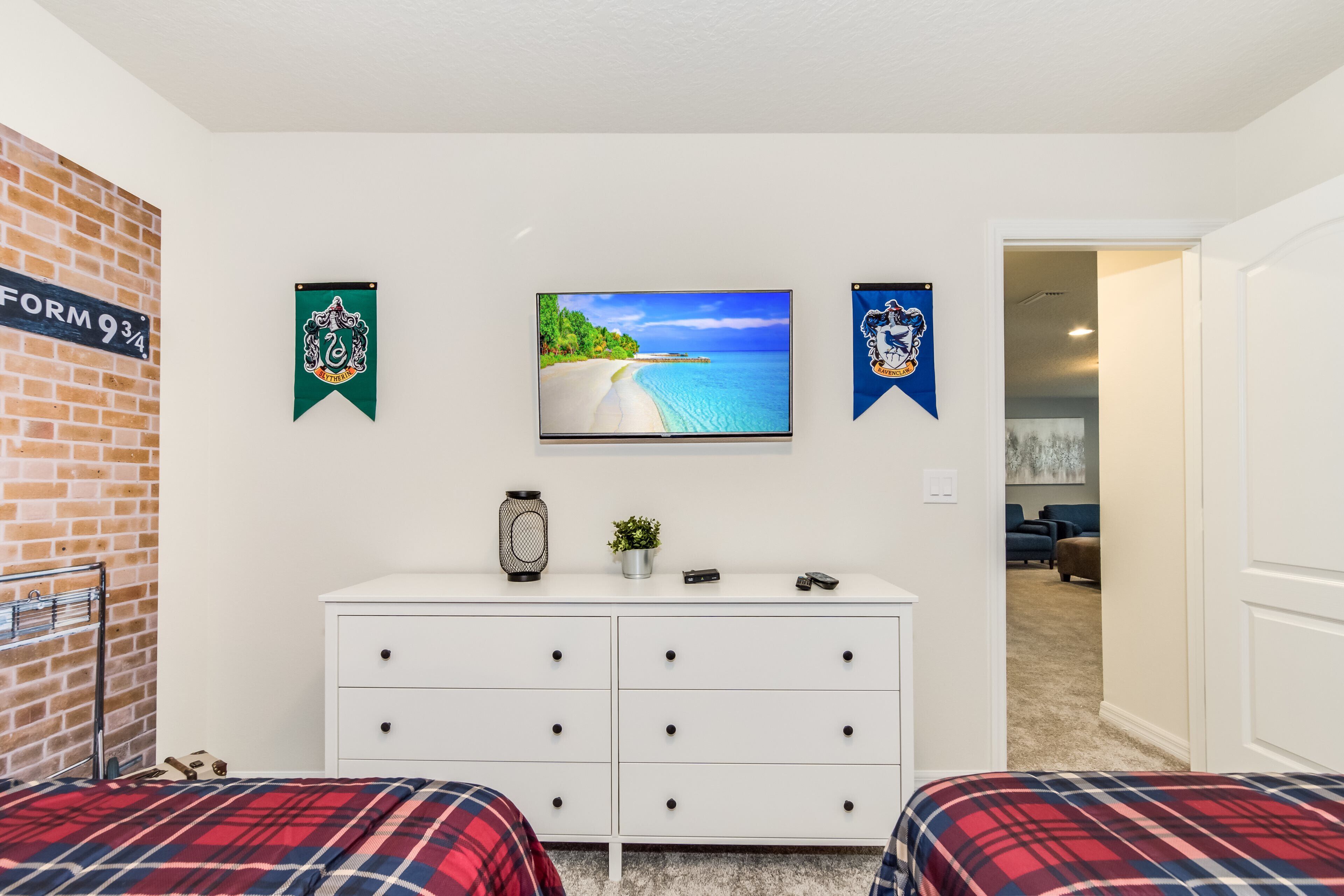 A bedroom with two beds, a dresser, a television, and a brick wall.