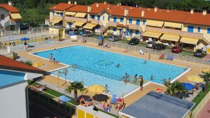 A swimming pool surrounded by multi-story buildings with balconies, a parking area, and a clear sky. - Residence Solmare Two-room apartment Bilo Superior for 4 persons (Rosolina Mare)