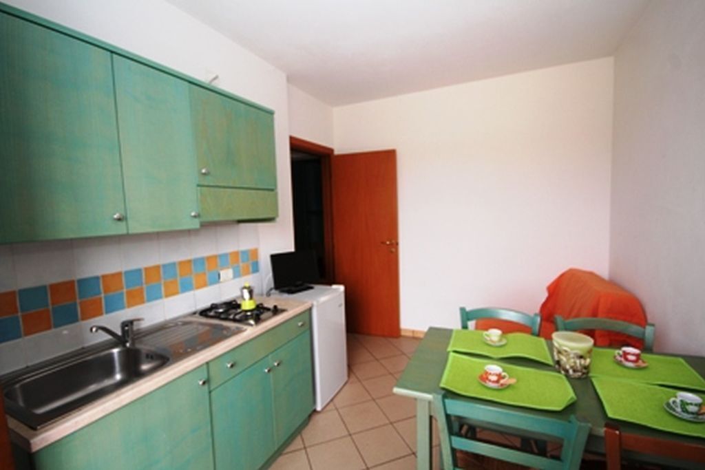 A compact kitchen with green cabinets, a sink, and a small refrigerator. There is a dining area with a green table and chairs.