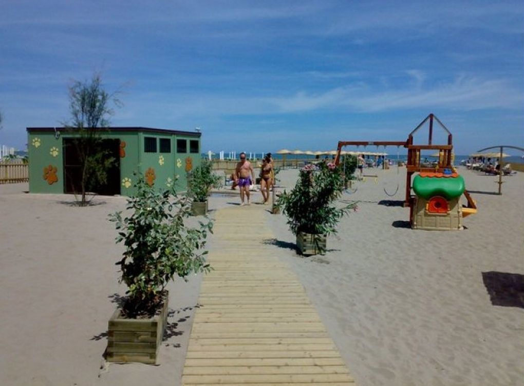 A wooden pathway leading to a beach area with a small green structure and a play area.
