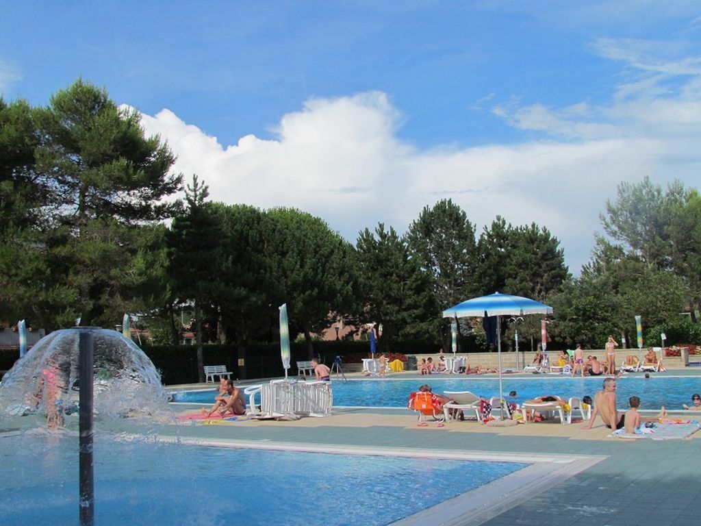 Un espace piscine doté de chaises longues et de parasols, entouré d’arbres.