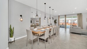A modern dining area with a long table set for six, white chairs, pendant lights, and a potted plant. - Last Minute Disney Getaway! Private Pool, Hot Tub & Game Room. Book Now! #42814 (Orlando)