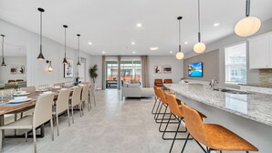 A modern kitchen with a marble countertop, a dining area with a long table and chairs, and pendant lighting. - Last Minute Disney Getaway! Private Pool, Hot Tub & Game Room. Book Now! #42814 (Orlando)