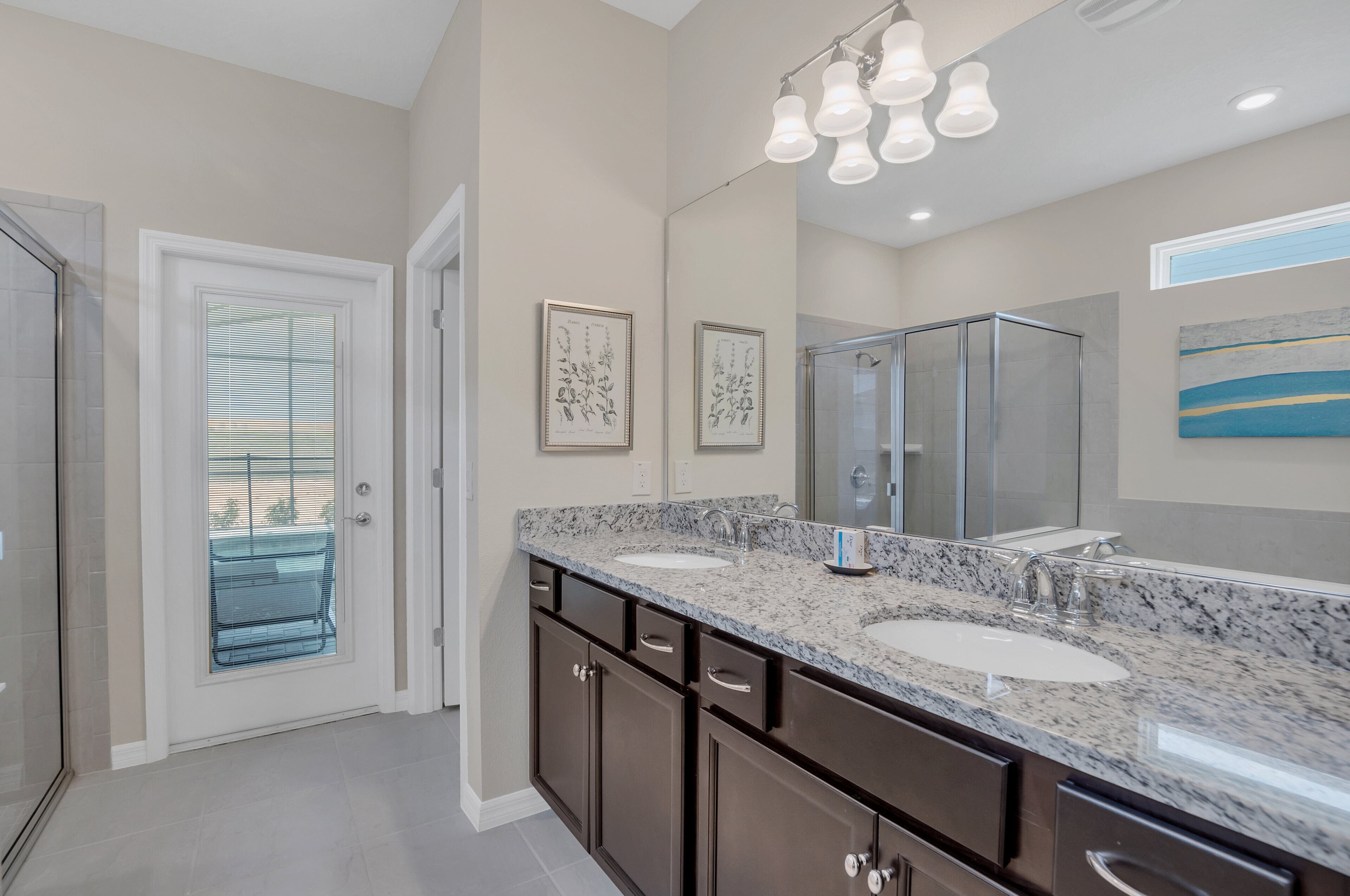 A modern bathroom with a large mirror, two sinks, dark cabinets, and a shower area.