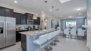 A modern kitchen with dark cabinets, stainless steel appliances, and a central island with bar stools.