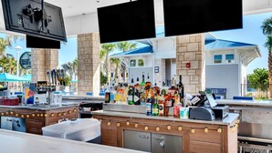 A bar area with a counter, multiple liquor bottles, a cash register, and two TVs mounted above the bar.