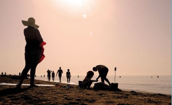 A beach scene with people walking and playing in the sand.