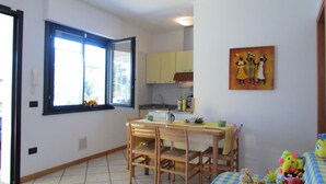 Eine kompakte Küche mit Essbereich, einem Fenster mit Jalousien und einem Bild an der Wand.