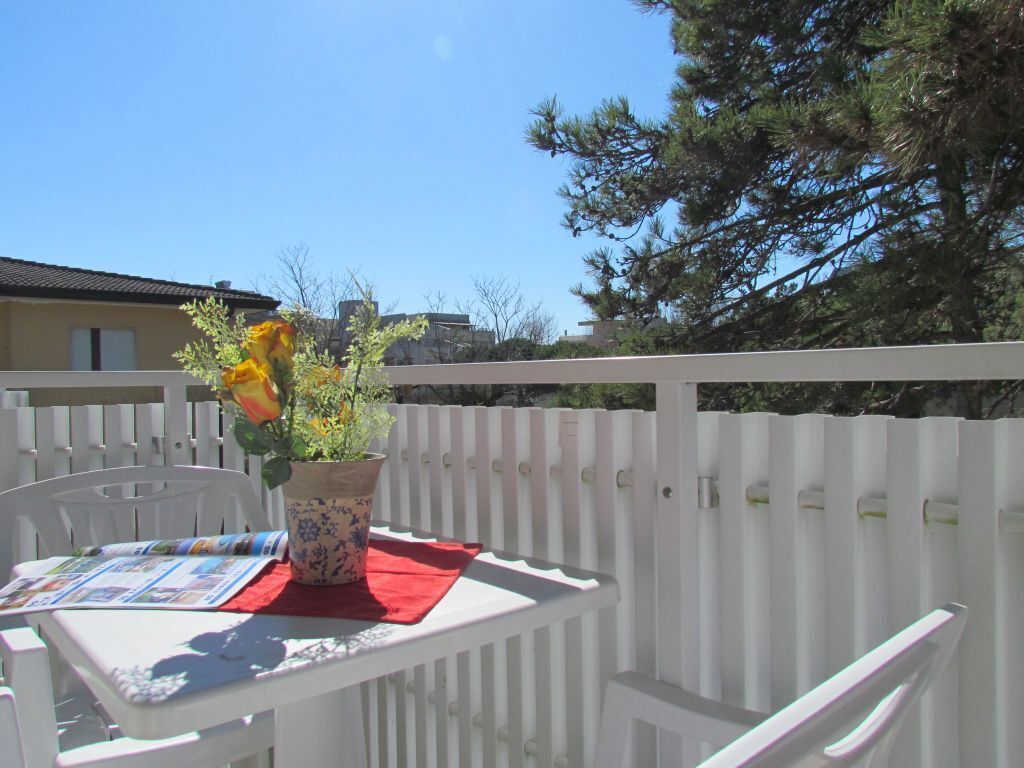 Een wit balkon met een tafel, een potplant en een rode doek.