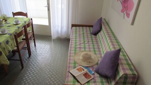 A room with a checkered sofa, a dining table with chairs, a window with curtains, and a wall with a flower painting. - Residenz Codan Wohnung Codan für 6 Personen (Bibione)