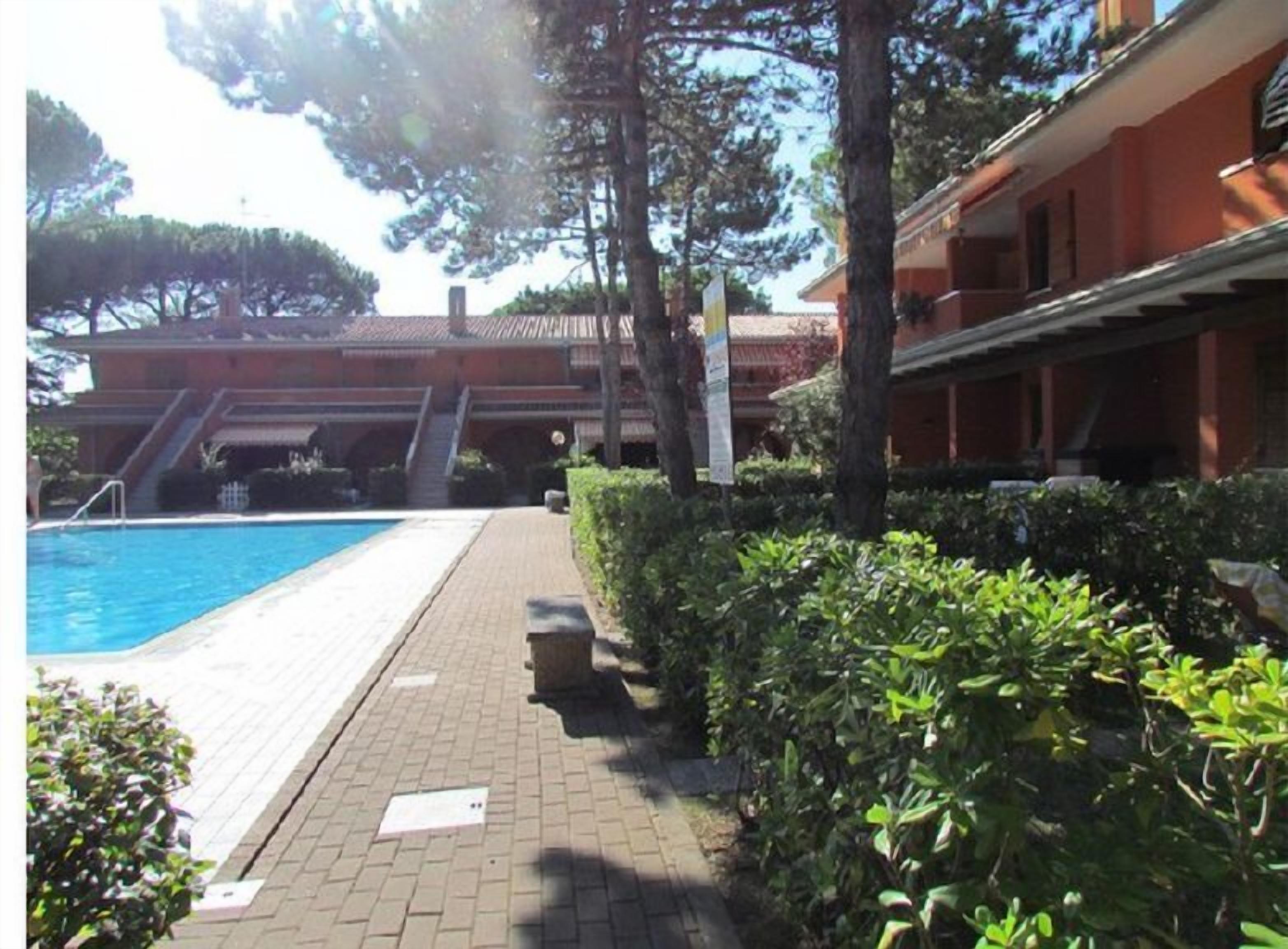 A swimming pool with a tiled deck, surrounded by well-maintained hedges and trees.