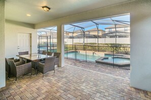 Une terrasse couverte avec une structure vitrée, une piscine et un coin repas aménagé avec des meubles en osier.