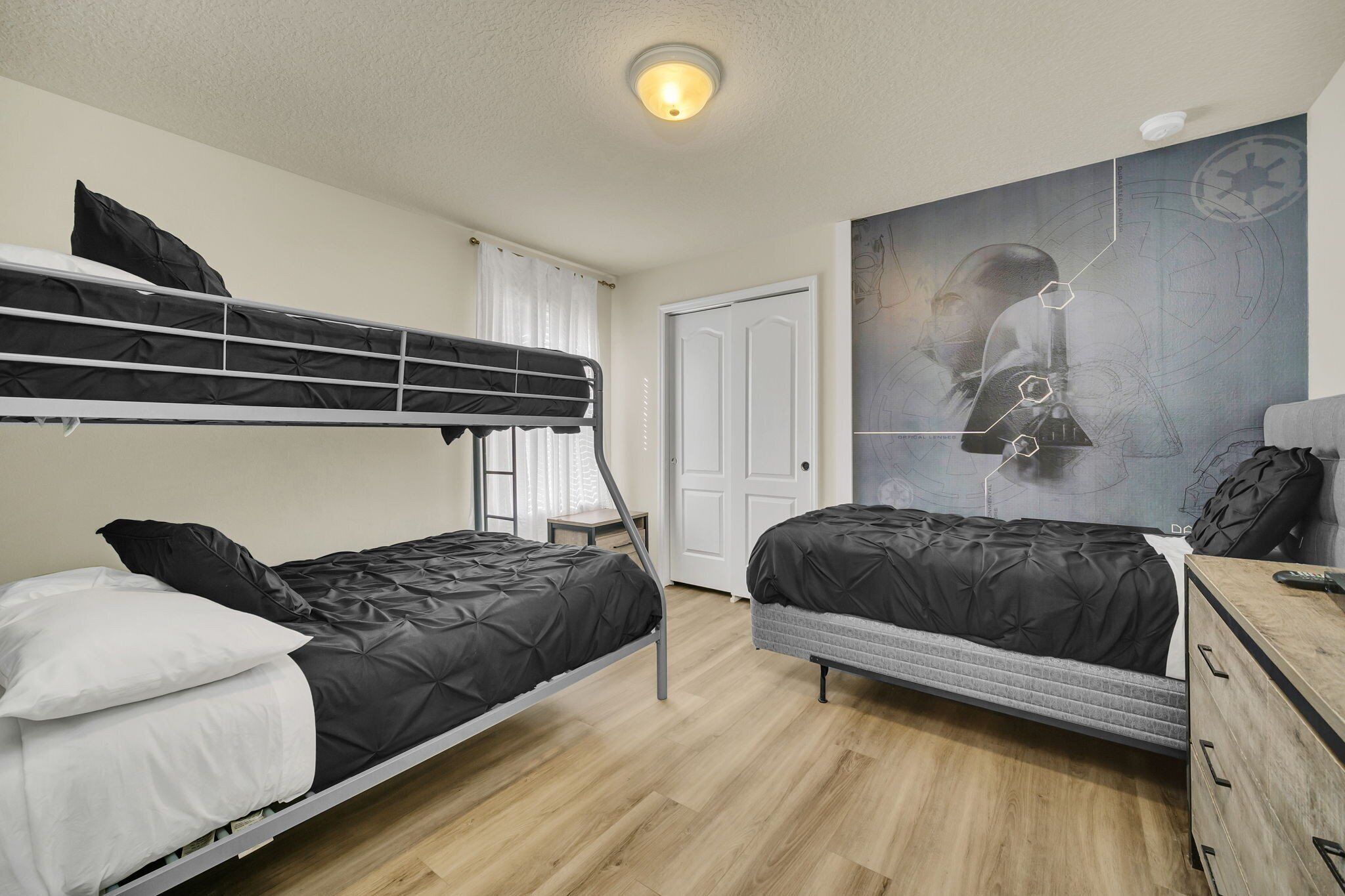 Une chambre de dortoir avec des lits superposés, un mur décoré sur le thème de Star Wars, une commode en bois et une porte blanche.