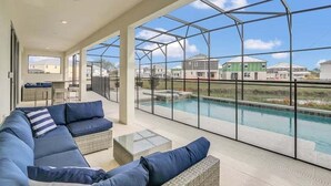 A spacious balcony with a glass enclosure, a pool, and a seating area with a sofa and chairs.
