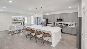 A modern kitchen with a large island, grey cabinets, stainless steel appliances, and a dining area with white chairs.