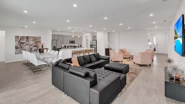 A spacious living area with a large sectional sofa, a dining table with chairs, and a kitchen in the background.