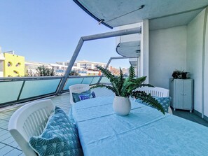 Un balcon avec une table, des chaises, un pot de fleurs et un meuble.