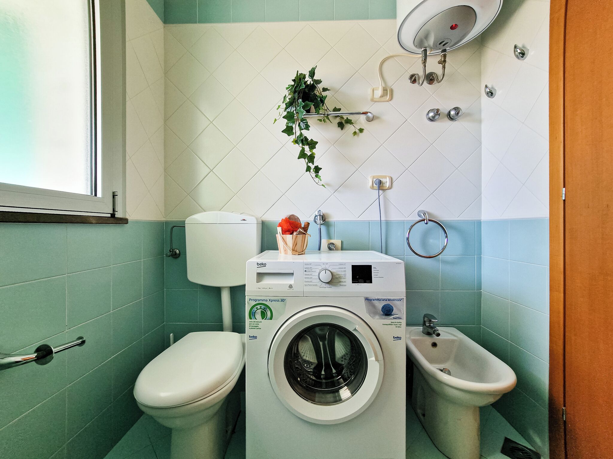 Un baño pequeño con lavadora, inodoro, bidé y ventana.
