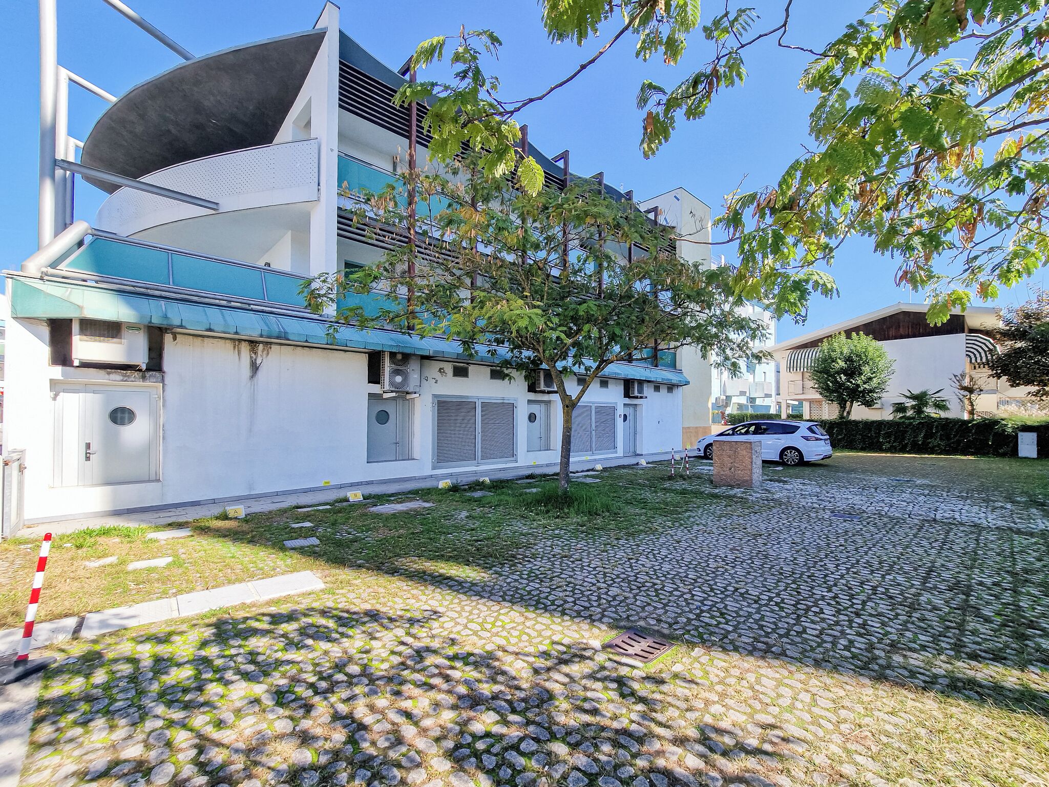 Un edificio moderno con techo plano, un gran ventanal y un árbol en primer plano.