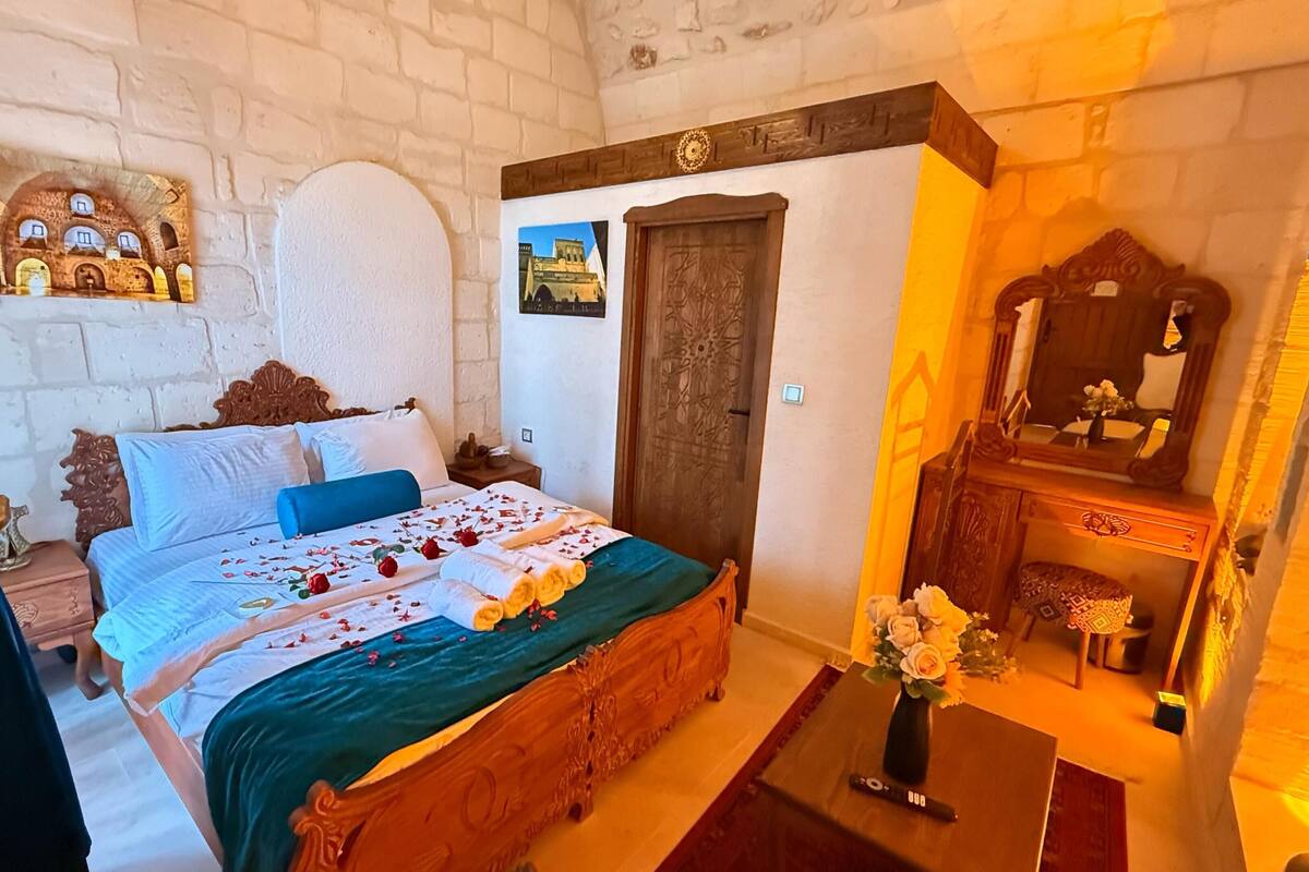 Een slaapkamer met een houten bed, nachtkastje, dressoir, spiegel en een aan de muur hangend schilderij.