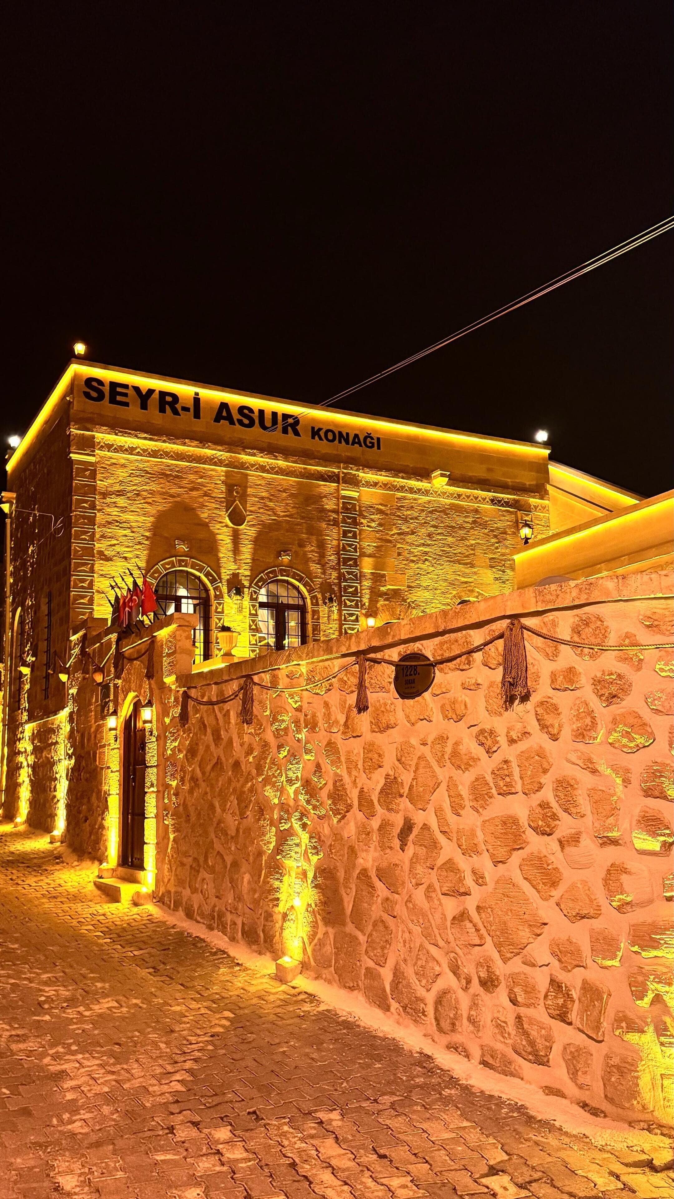 A stone building with a sign reading "SEYRI ASUR KONAGI" at night.