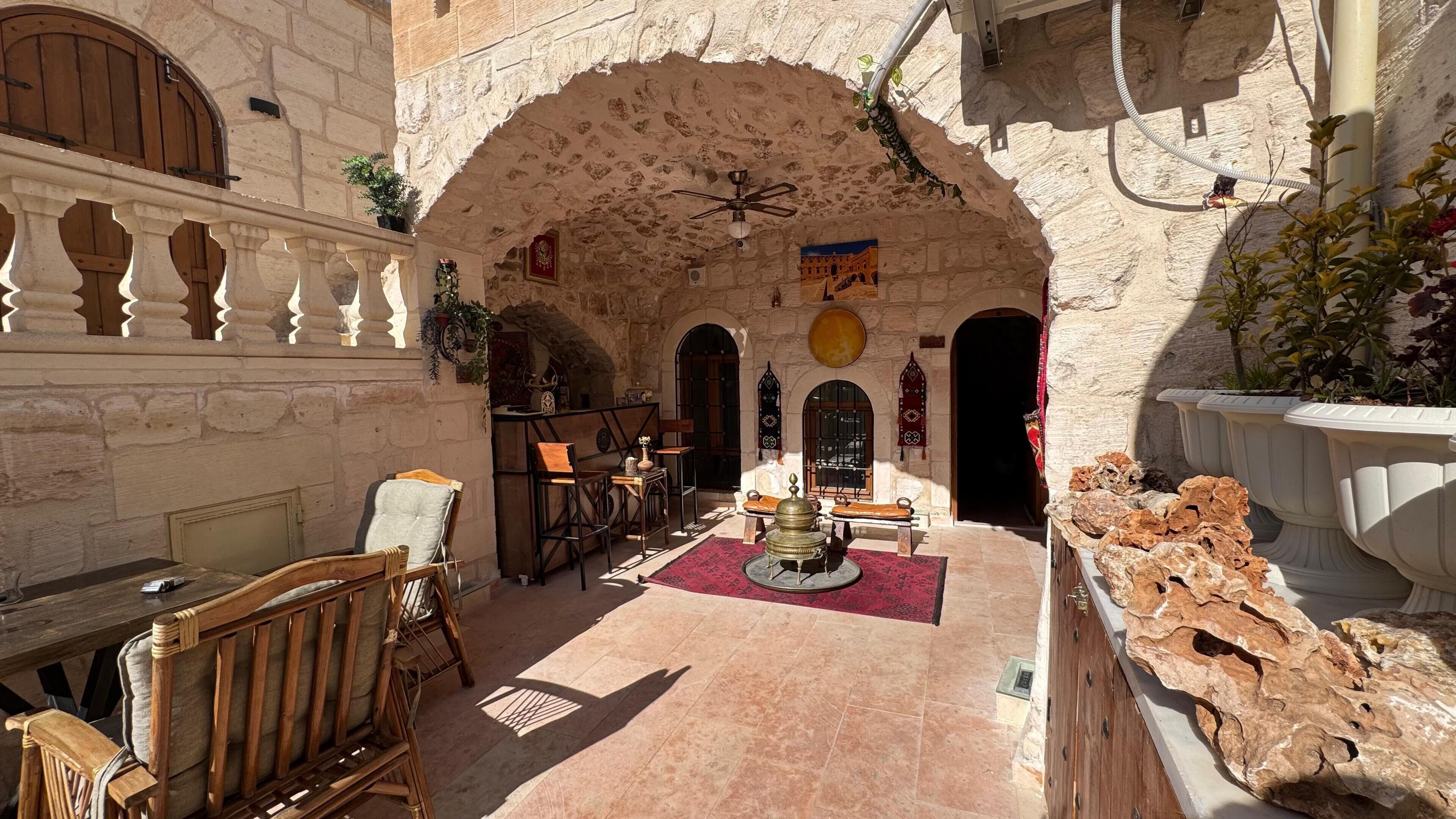 A stone-walled courtyard with a fountain, wooden furniture, and a tiled floor.
