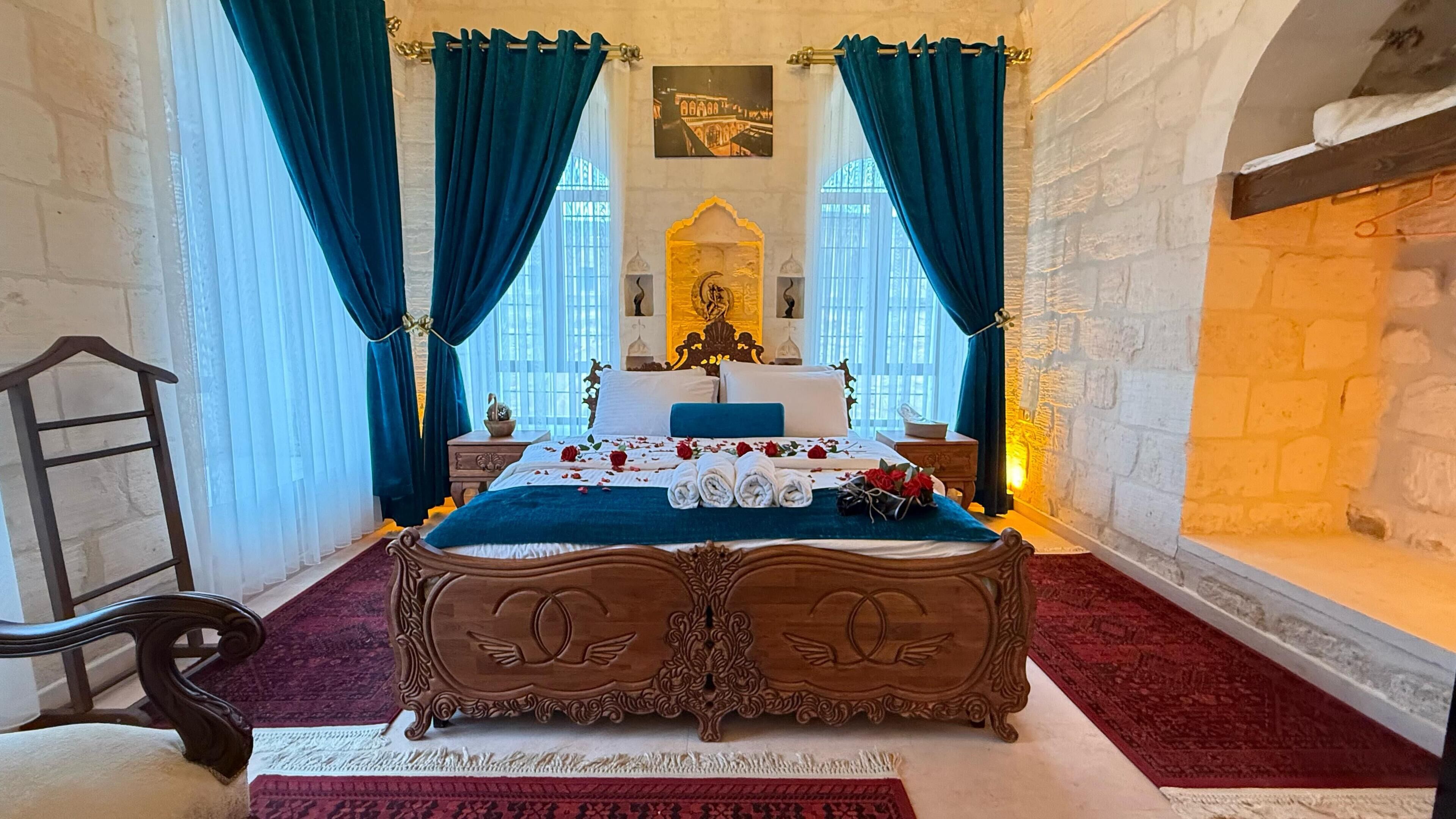 A room with a large bed, a wooden headboard, a red carpet, and a stone wall.