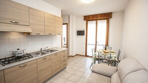 Cocina compacta con estufa a gas, pileta y muebles de madera. Cuenta con un comedor con mesa y sillas, además de un sofá en una esquina.