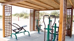 Un gimnasio al aire libre con equipo de ejercicio bajo una pérgola de madera.