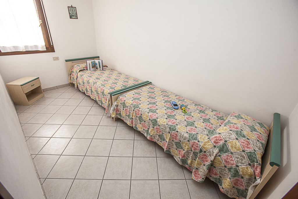 A small, clean room with a single bed, a bedside table, and a window.