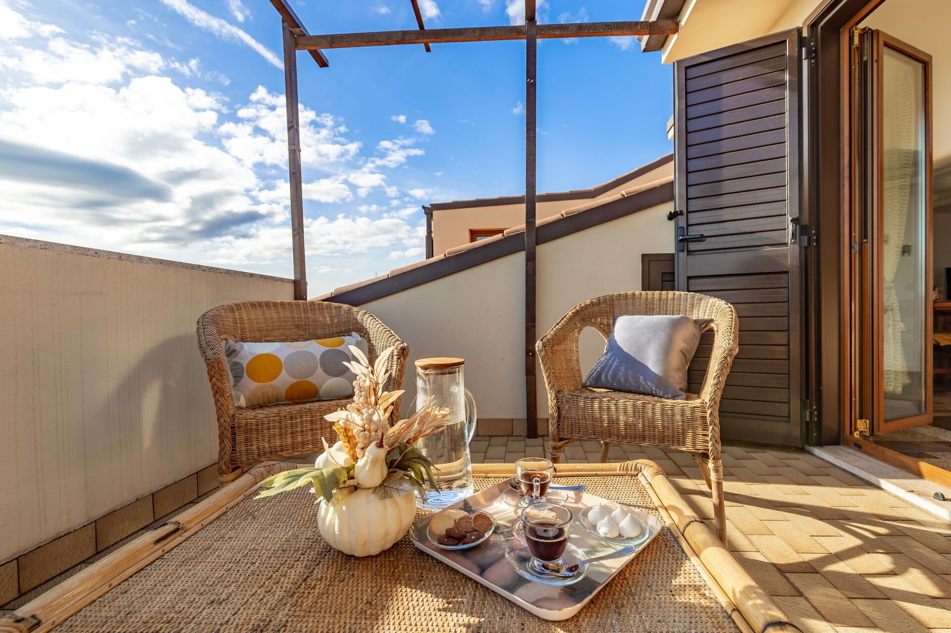 A balcony with wicker chairs, a tray with snacks and drinks, and a decorative vase.