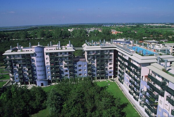 A high-rise hotel with multiple balconies, a rooftop pool, and a view of the surrounding greenery and distant landscape.