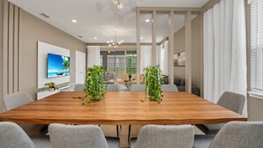 A conference room with a wooden table, grey chairs, a large chandelier, and potted plants.