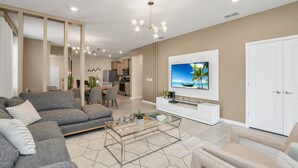 A modern living room with a grey sectional sofa, a glass coffee table, and a flat-screen TV mounted on the wall.