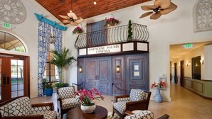 Un hall d’entrée avec une enseigne indiquant « Paradise Palms Cinema », un espace salon avec des fauteuils à motifs, des plantes en pot et un ventilateur de plafond.