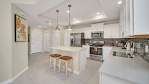 Una cocina moderna con armarios blancos, electrodomésticos de acero inoxidable y una isla central con taburetes.