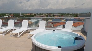 Eine Dachterrasse mit Whirlpool, weißen Liegestühlen und Blick auf die Stadt.