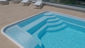 Ein Swimmingpool mit klarem, blauem Wasser, umgeben von weißen Liegestühlen und einer gefliesten Terrasse.