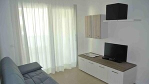 Ein modernes Wohnzimmer mit grauem Sofa, einem Fernseher auf einer Holzkommode und einem weißen Vorhang.