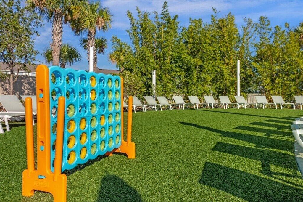 A pool area with a blue and orange inflatable game structure, white lounge chairs, and green artificial grass.