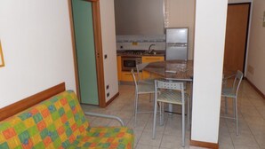 Un espacio habitable compacto con kitchenette, una zona de comedor con mesa y sillas, y un sofá colorido.