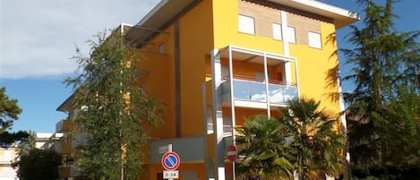 Un edificio amarillo con balcón, rodeado de follaje y palmeras.
