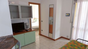 Una habitación con cama, escritorio, televisión y kitchenette.