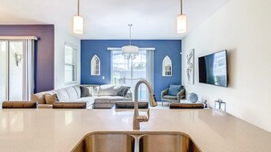 Una cocina moderna con un lavamanos doble, un comedor con mesa y sillas, y una sala de estar con sofá y televisor.