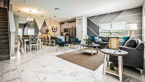A modern living room with a dining area, a kitchen in the background, and a staircase leading to another level. - Last Minute Disney Getaway! Townhouse with Private Pool. Book Now! #87939 (Orlando)